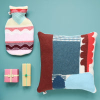 donna wilson abstract knitted cushion in blues and reds laid flat with hot water bottle