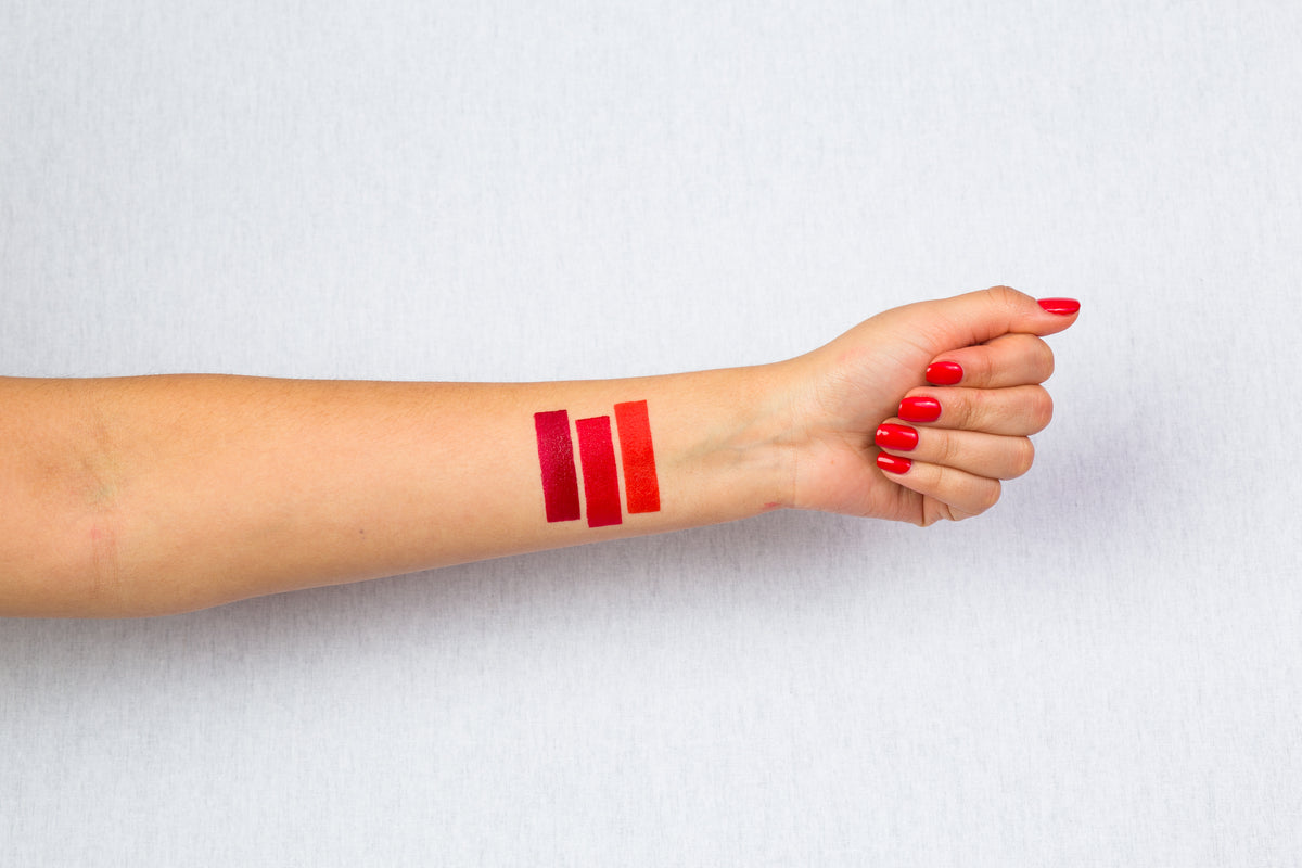 pale skin arm with red nails and three stripes of different coloured red lipsticks to show shade