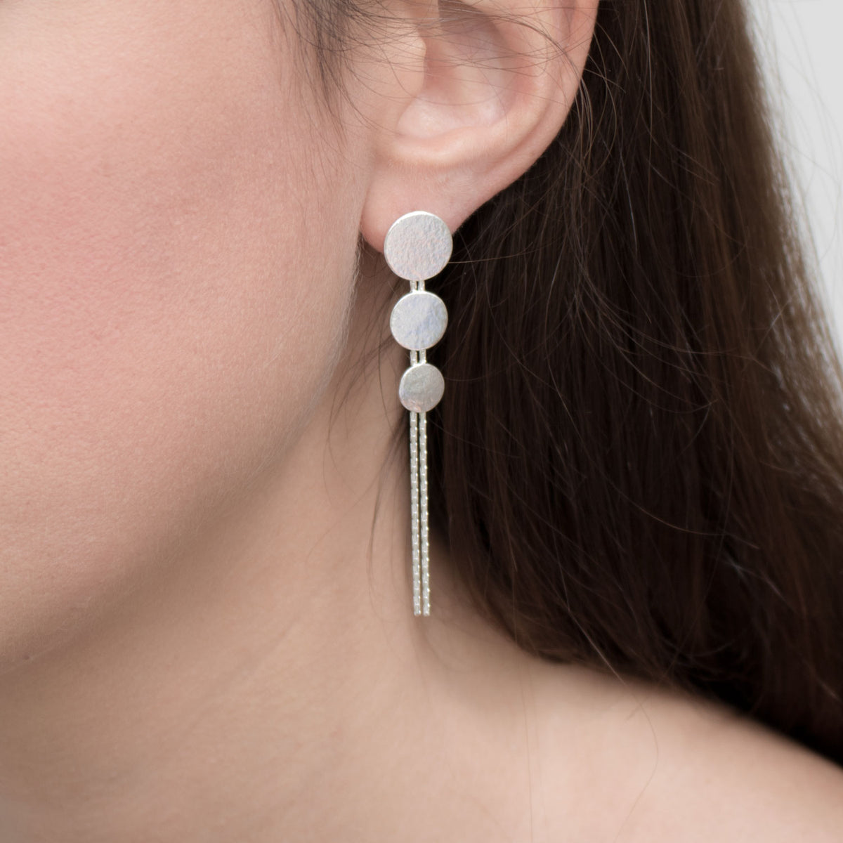 Silver triple disc drop earrings by British jewellery designer Cara Tonkin model