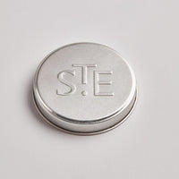 photo of tin candle lid with embossed letter STE from St Eval Candles